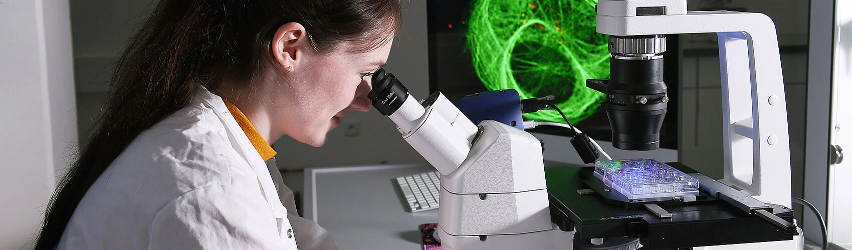 Frau die durch ein Mikroskop schaut