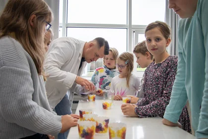 Das Bild zeigt Kinder mit einem Lehrenden, der gerade ein Experiment durchführt.