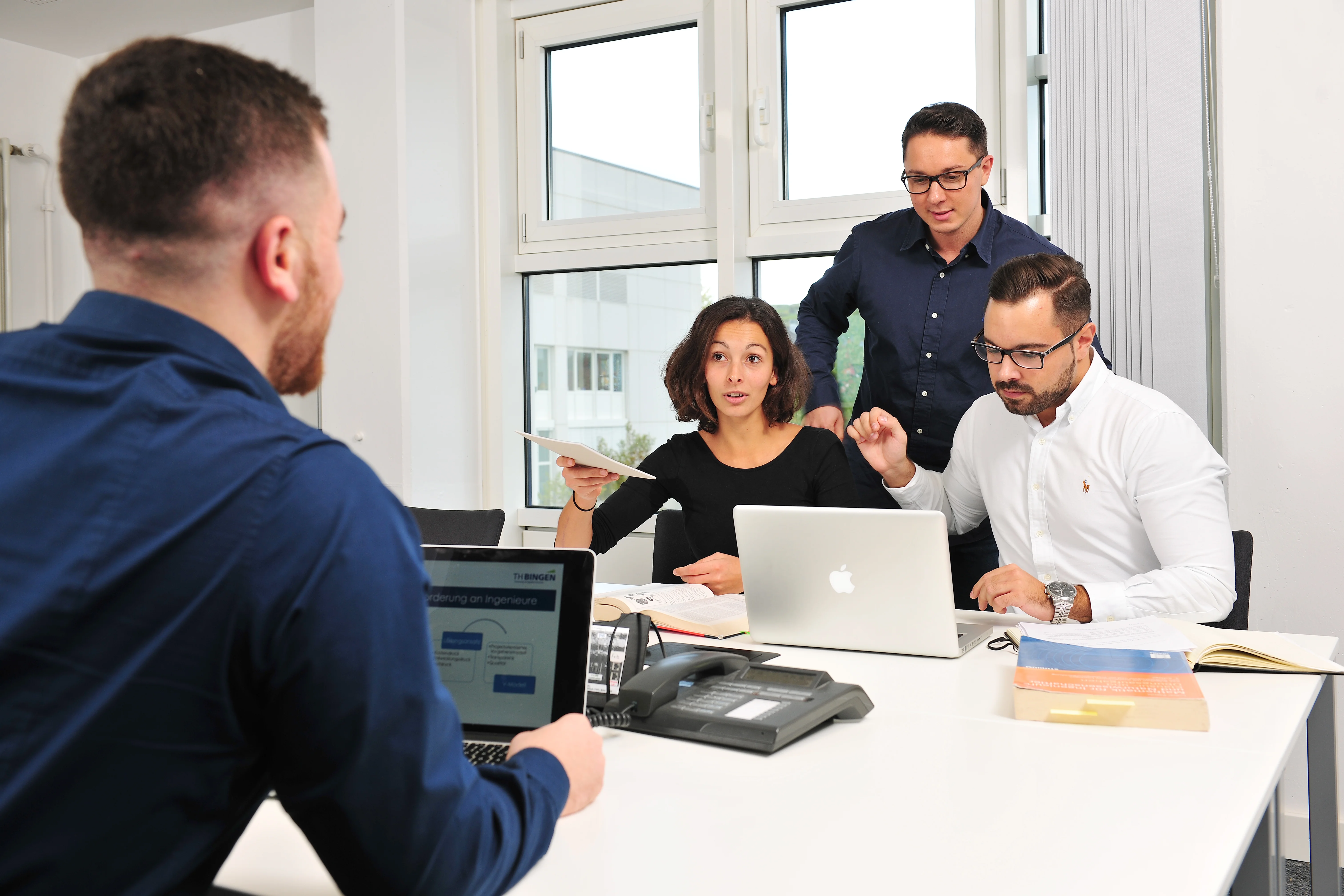 Das Bild zeigt drei Männer und eine Frau, die an einem Tisch sitzen und sich mit Lehr- und Lernmaterialien austauschen.