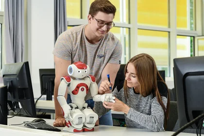 Zwei Studierende arbeiten mit einem Roboter 