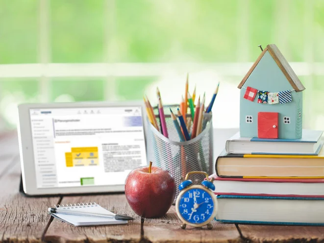 Schreibtisch mit Tablet, Bücherstapel, Wecker und Apfel