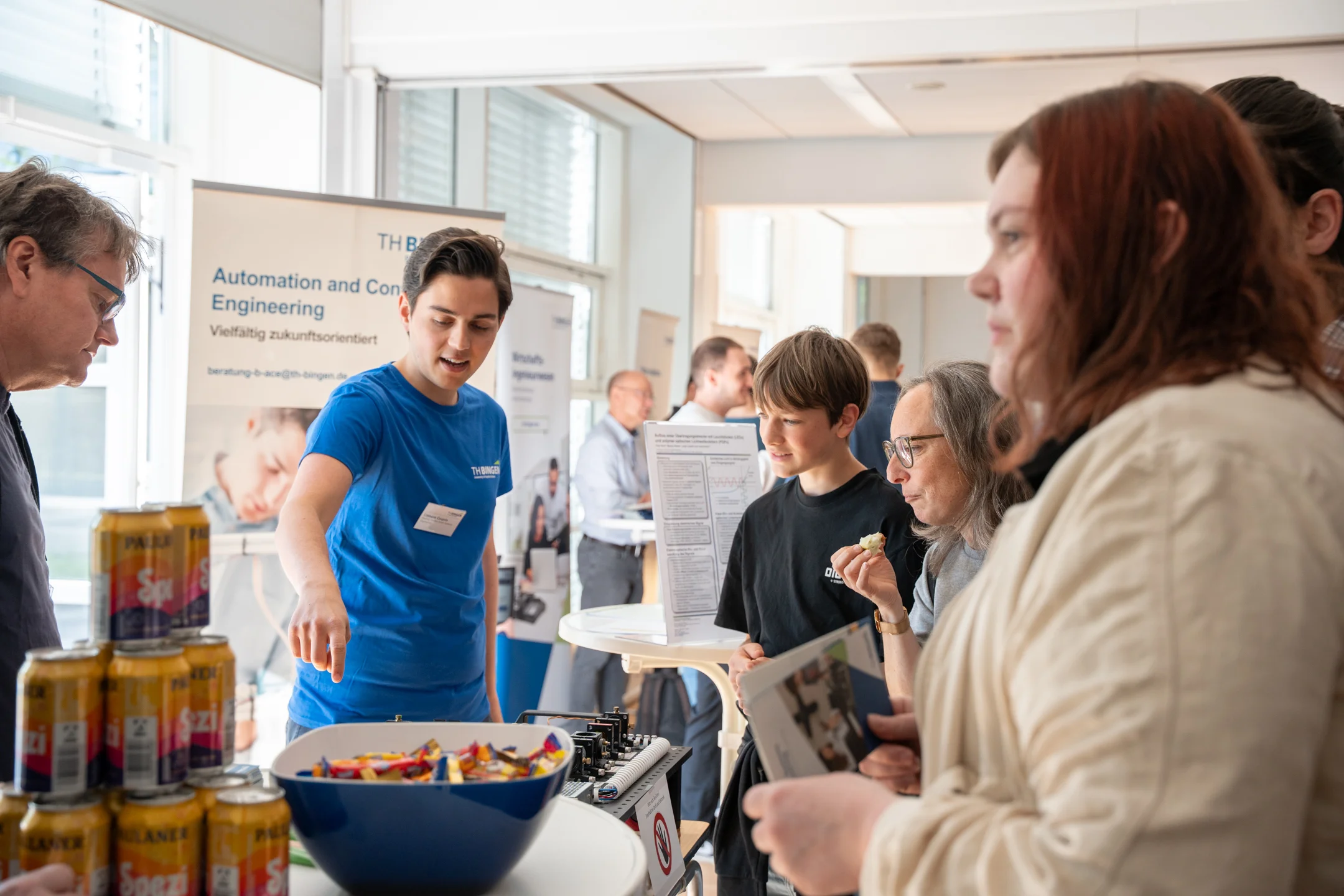 Das Bild zeigt TH-Mitarbeitende, die den Besucher*innen etwas am Stand erklärt.