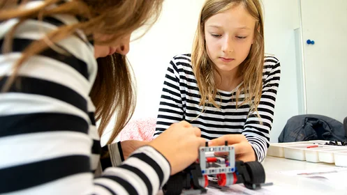 Das Bild zeigt zwei Mädchen, die an einem Modellauto werkeln.