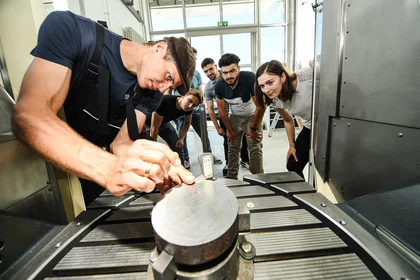 Ein Dozent zeigt Studierenden etwas an einer Maschine.