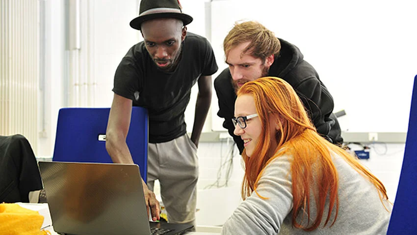 3 Studierenden an einem Laptop